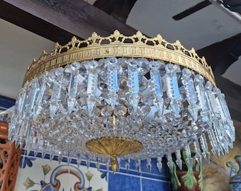 May include: A gold-toned chandelier with a round, ornate frame and crystal prisms hanging from it. The chandelier is illuminated and casts a warm glow.