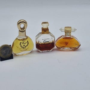 Op de afbeelding: Drie miniatuur parfumflesjes. De fles links is geel met een gouden dop en de tekst "First de Cleef & Arpels Paris". De middelste fles is helder met een bruine vloeistof en de tekst "Gem eau de toilette". De fles rechts is oranje met een gouden dop en de tekst "Ola!".
