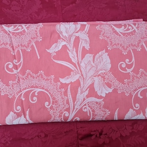 Könnte beinhalten: Ein rosa Stoff mit einem weißen Blumenmuster. Der Stoff zeigt ein sich wiederholendes Muster aus stilisierten Blumen und Blättern.