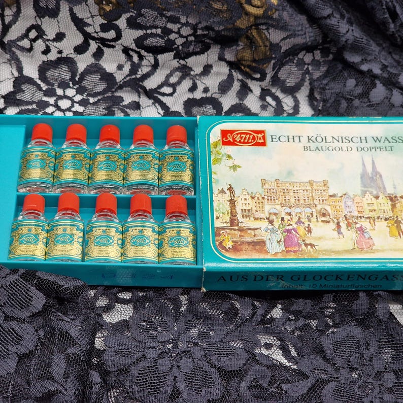 May include: A vintage set of 10 miniature bottles of Echt K&ouml;lnisch Wasser, each with a red cap and a teal and gold label. The bottles are arranged in a teal box with a picture of a European town.