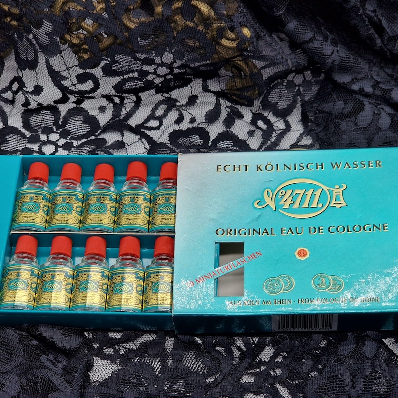 May include: A teal box containing twelve miniature bottles of Eau de Cologne. Each bottle has a gold label and a red cap. The box is labeled "Echt K&ouml;lnisch Wasser" and "Original Eau de Cologne".