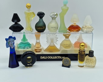 May include: A collection of miniature perfume bottles in various shapes and colors, displayed on a clear shelf. The bottles include a black geometric design, a blue figure, and bottles with gold accents. The text "DALI COLLECTION" is visible.