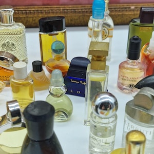 K&ouml;nnte beinhalten: Eine Sammlung von Miniatur-Parf&uuml;mflaschen in verschiedenen Formen und Gr&ouml;&szlig;en. Die Flaschen enthalten unterschiedlich farbige Fl&uuml;ssigkeiten, darunter Gelb, Klar und Rosa. Einige Flaschen haben schwarze, silberne oder blaue Verschl&uuml;sse. Das Bild zeigt eine Vielzahl von Vintage-Parf&uuml;mflaschen.