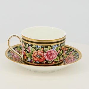Puede incluir: Una taza de té y un platillo blancos con un patrón floral negro y un borde dorado. El patrón floral presenta flores rosas, rojas y amarillas.