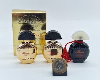 May include: A collection of miniature perfume bottles, including two gold-colored bottles with black fan-shaped tops and one black bottle with a white top. The bottles are labeled "Theosiris Parfum" in red script. A gold box with a fan design is in the background.