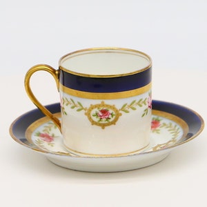 Könnte beinhalten: Eine weiße Porzellan-Teetasse und -Untertasse mit blauem und goldenem Rand und floralem Design. Die Tasse hat einen goldenen Henkel.