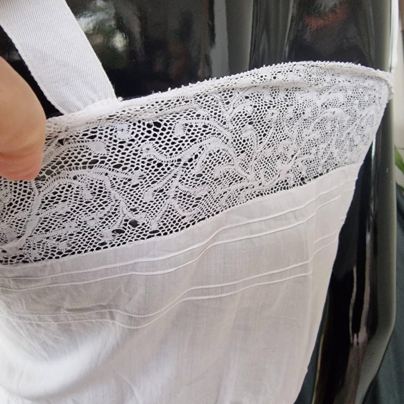 May include: Close-up of a white camisole with a delicate lace trim. The camisole features a simple design with a white strap and a detailed lace border. The fabric appears to be soft and lightweight, suitable for lingerie or layering.