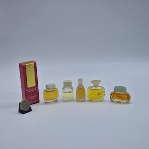 May include: A selection of miniature perfume bottles in different designs. The bottles are filled with a yellow liquid and are displayed with a pink and gold box labelled "Beautiful". A coin is also present.