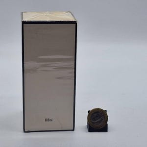 May include: A rectangular box with a light beige front and black trim. The box is wrapped in clear plastic. The text "118ml" is printed on the front. A coin is next to the box.