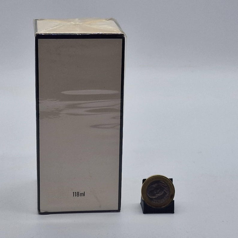 May include: A rectangular box with a light beige front and black trim. The box is wrapped in clear plastic. The text "118ml" is printed on the front. A coin is next to the box.