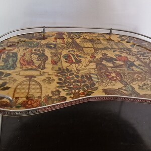 Könnte beinhalten: Ein vintage Silbertablett mit einem dekorativen, farbenfrohen und detaillierten Druck einer mittelalterlichen Szene. Das Tablett hat eine geschwungene Form und einen silbernen Metallrand. Das Tablett steht auf einem silbernen Metallständer mit drei Beinen.