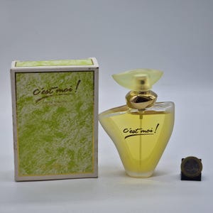Peut inclure: Un ensemble de parfum avec flacon et boîte. Le flacon de parfum a une forme unique avec un liquide jaune à l'intérieur. Le flacon a un bouchon vert clair et des détails dorés. La boîte est verte avec l'inscription "C'est moi!"