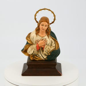 Puede incluir: Una estatua de madera de una persona con una corona de espinas, vestida con una túnica blanca y dorada con una capa azul y verde. La estatua está sobre una base de madera.