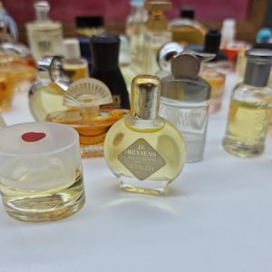 K&ouml;nnte beinhalten: Eine Sammlung von Vintage-Parf&uuml;mflaschen in verschiedenen Formen und Gr&ouml;&szlig;en. Die Flaschen sind mit einer gelben Fl&uuml;ssigkeit gef&uuml;llt. Eine Flasche hat einen goldenen Verschluss und ein Etikett mit der Aufschrift "Je Reviens Worth".