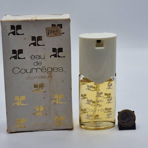 May include: A vintage Eau de Courr&egrave;ges atomizer perfume bottle with its original box. The box is off-white with gold-colored logos and text. The perfume bottle is clear with a cream-colored top and contains a yellow liquid. A coin is next to the bottle.