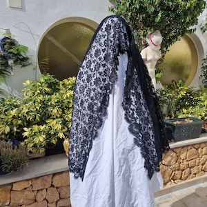 May include: A black lace shawl with a floral pattern. The shawl is draped over a white garment.