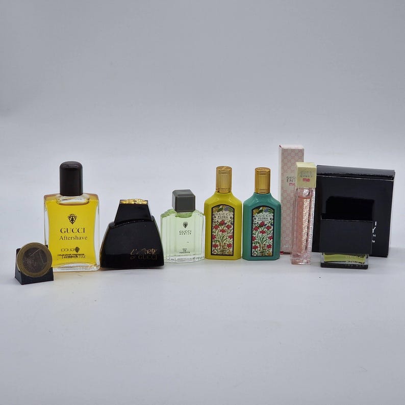 May include: A collection of Gucci fragrances and aftershave bottles in various shapes and sizes. The bottles are in shades of yellow, black, green, and pink. Some bottles have floral designs, and one has a coin next to it.