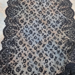 May include: Black lace fabric with a floral pattern. The lace has a scalloped edge.