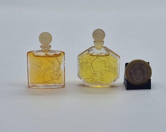 Puede incluir: Dos frascos de perfume antiguos con diseños florales y geométricos. Los frascos contienen un líquido amarillo y tienen tapones transparentes. Una moneda está al lado de los frascos para comparar el tamaño. Los frascos están sobre una superficie blanca.