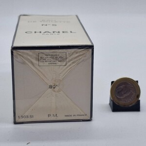 May include: A rectangular box of Chanel No. 5 Eau de Toilette, with the brand name in black letters. The box is off-white with black trim and text. A coin is next to the box. The box is Made in France.