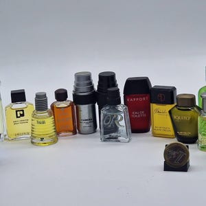 May include: A collection of miniature perfume bottles in various shapes, sizes, and colors. The bottles have different colored caps and labels, with some featuring text. The bottles are arranged on a white surface.