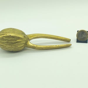 May include: A gold-colored metal nutcracker shaped like a walnut. The nutcracker is about 5 inches long and has a textured surface.