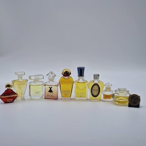 Può includere: Una collezione di flaconi di profumo in miniatura di varie forme e dimensioni. I flaconi sono riempiti con liquidi di diversi colori, che vanno dal trasparente all'ambra. Alcuni flaconi hanno tappi dorati o argentati, mentre altri presentano design unici. I flaconi sono disposti in fila.