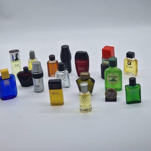 May include: A collection of miniature perfume bottles in various shapes, sizes, and colors. The bottles include blue, green, yellow, black, and clear glass. Some bottles have labels, and others have unique cap designs. The bottles are arranged on a white surface.
