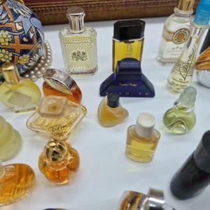 K&ouml;nnte beinhalten: Eine Sammlung von Miniatur-Parf&uuml;mflaschen in verschiedenen Formen und Gr&ouml;&szlig;en. Die Flaschen sind mit unterschiedlich farbigen Fl&uuml;ssigkeiten gef&uuml;llt, darunter Gelb, Orange und Klar. Einige Flaschen haben aufwendige Designs und Etiketten, andere sind schlicht und elegant.