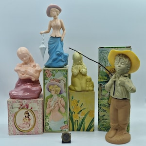 Könnte beinhalten: Sammlung von Vintage-Keramikfiguren, darunter eine Frau in einem rosa Kleid, eine Frau in einem blauen Kleid mit einem Regenschirm, ein betendes Kind und ein Junge mit einer Angelrute. Die Figuren werden mit ihren Originalverpackungen präsentiert.