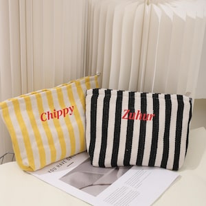 May include: Two striped fabric pouches with zipper closures. The pouch on the left is yellow and white with the word "Chippy" embroidered in red. The pouch on the right is black and white with the word "Zuhur" embroidered in red.