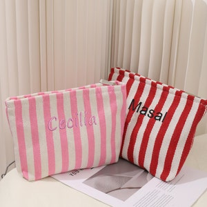 May include: Two striped zippered pouches, one pink and white with the name "Cecilia" embroidered on it, and one red and white with the name "Masal" embroidered on it.