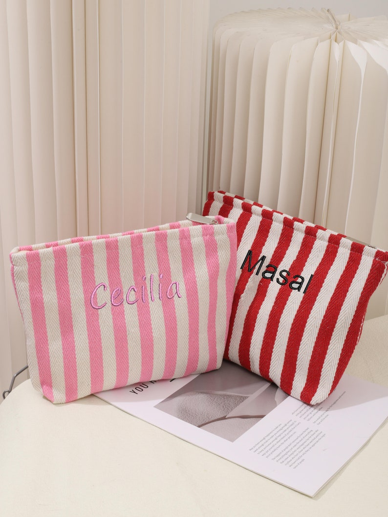 May include: Two striped zippered pouches, one pink and white with the name "Cecilia" embroidered on it, and one red and white with the name "Masal" embroidered on it.