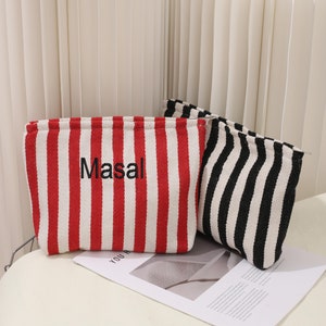May include: Two striped fabric pouches. One pouch is red and white with the word "Masal" embroidered on it. The other pouch is black and white.