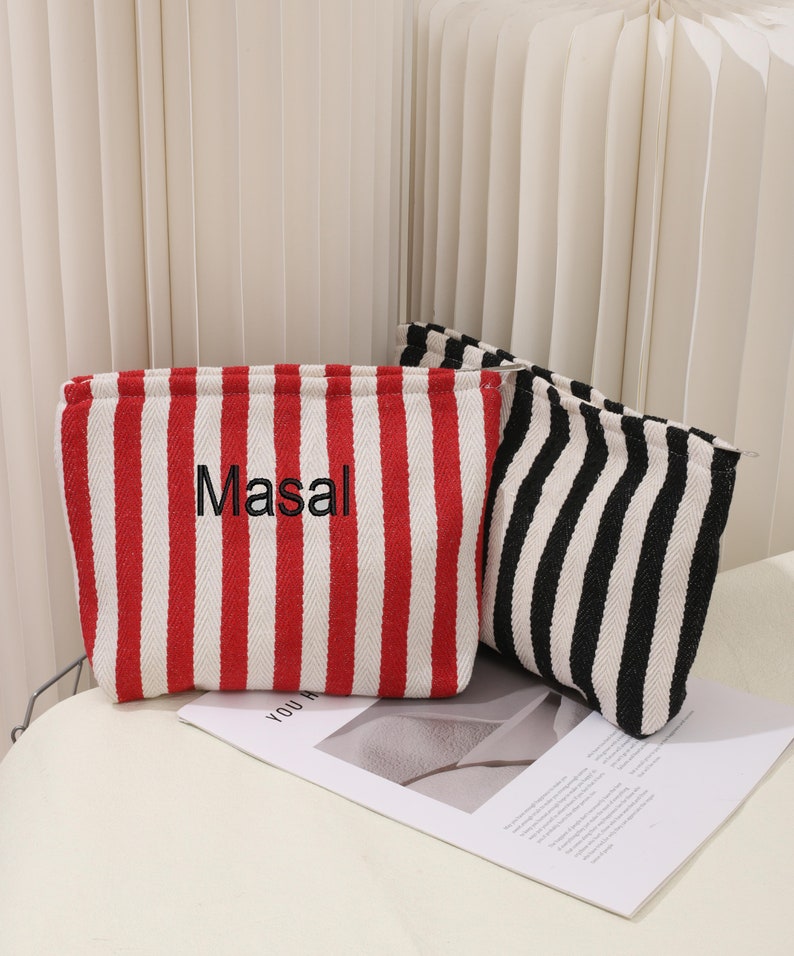 May include: Two striped fabric pouches. One pouch is red and white with the word "Masal" embroidered on it. The other pouch is black and white.