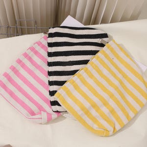 May include: Three striped fabric tote bags. One is pink and white, one is black and white, and one is yellow and white.