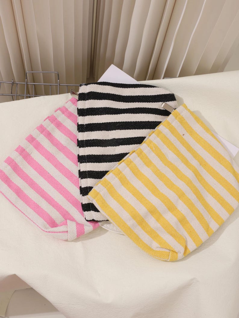 May include: Three striped fabric tote bags. One is pink and white, one is black and white, and one is yellow and white.