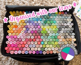 May include: A black carrying case filled with a large collection of upright markers in a wide spectrum of colors. The markers are arranged in rows, each featuring a color-coded cap with printed labels. Text on the image reads Organised with our trays and New limited colours.