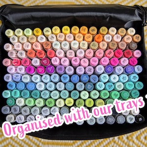 May include: A black case packed with a vibrant array of art markers, neatly arranged by colour. The markers span a spectrum from yellow to green. The image includes the text "Organised with our trays".