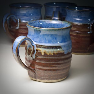 May include: Handmade ceramic mugs with a blue and brown glaze. The mugs have a ribbed texture on the lower half and a smooth, glossy finish on the upper half. The handles are curved and sturdy. A set of mugs for coffee or tea.