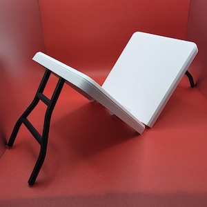 May include: A white folding table with black metal legs. The table is rectangular and has a smooth surface. The legs are curved and provide support. The table is designed to be portable and easy to set up.