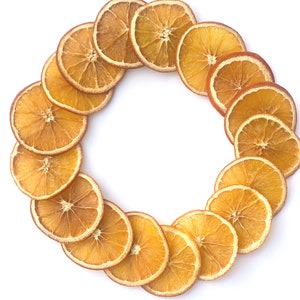 May include: A circular arrangement of dried orange slices, showcasing a vibrant orange hue with a lighter, almost translucent center. The slices are arranged in a ring against a clean white background, highlighting their natural texture and color.