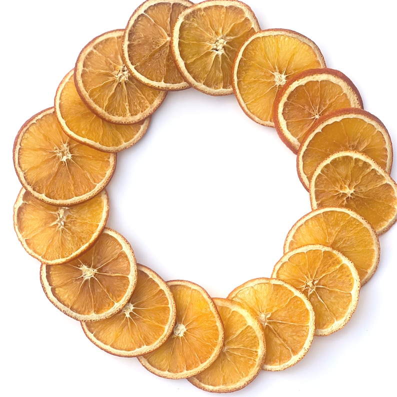May include: A circular arrangement of dried orange slices, showcasing a vibrant orange hue with a lighter, almost translucent center. The slices are arranged in a ring against a clean white background, highlighting their natural texture and color.