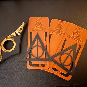 May include: Four orange bookmark with a black silhouette of a wizard's hat and the Deathly Hallows symbol. The bookmarks are made of a flexible plastic material.