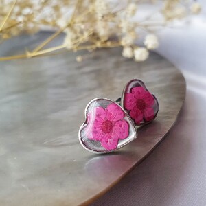 May include: A pair of silver heart-shaped earrings with a pink pressed flower inside each one.