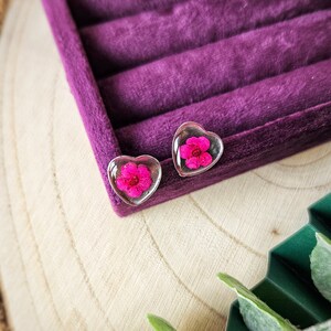 May include: A pair of heart-shaped earrings with a pink flower pressed inside each clear resin heart.