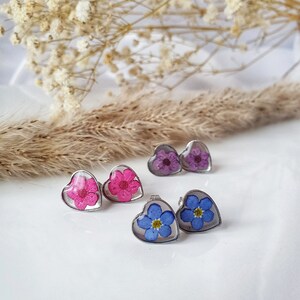 May include: Three pairs of heart-shaped earrings with pressed flowers inside. The earrings feature pink, purple, and blue flowers.