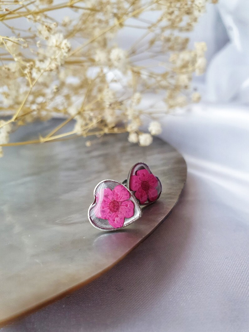 May include: A pair of silver heart-shaped earrings with a pink pressed flower inside each one.
