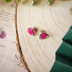 May include: A pair of heart-shaped earrings with pink pressed flowers inside. The earrings are silver and have a post back.