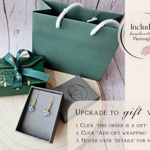 May include: A green gift bag with white handles, a green gift box with a green ribbon, a small gray box with a pair of blue heart-shaped earrings, and a sign that says "Upgrade to gift wrap: 1. Click "This order is a gift" 2. Click "Add gift wrapping" 3. Hover over "Details" for more info".